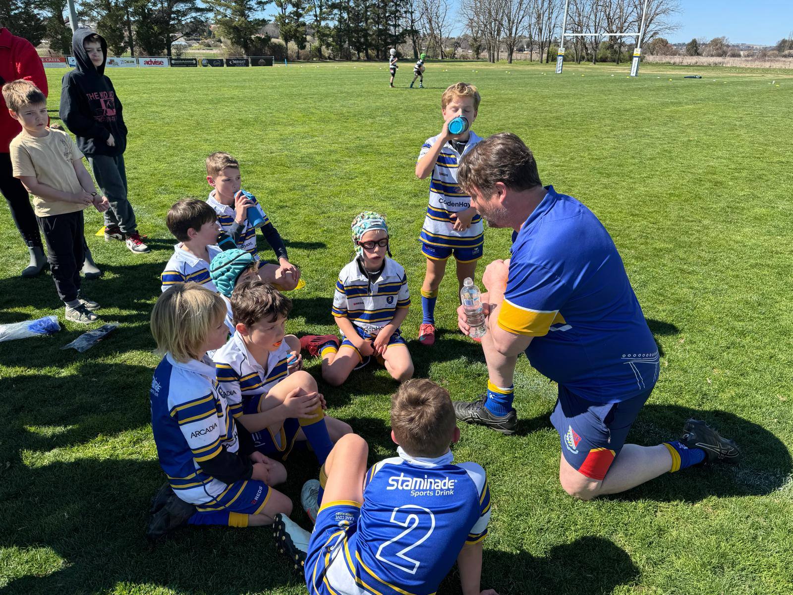Lane Cove Minis coach speaking to a seated team on the grass at Bathurst