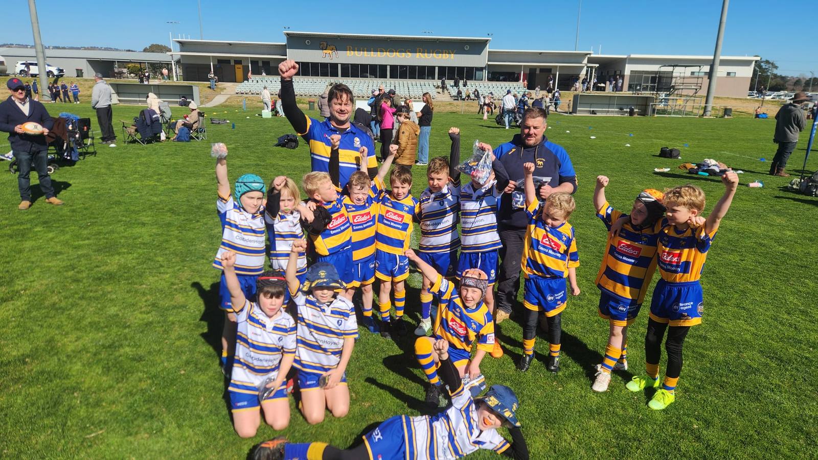 Lane Cove Minis players and coaches celebrating on the field in front of the Bathurst Bulldogs Rugby clubhouse
