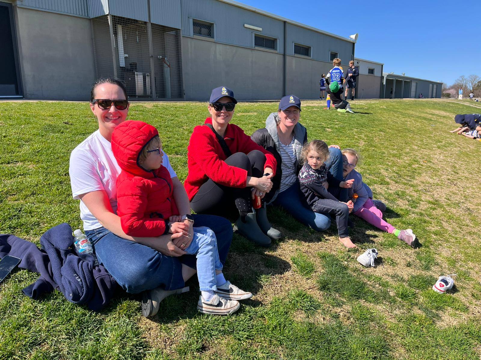 Lane Cove parents and siblings sitting on the sideline in the sunshine at Bathurst